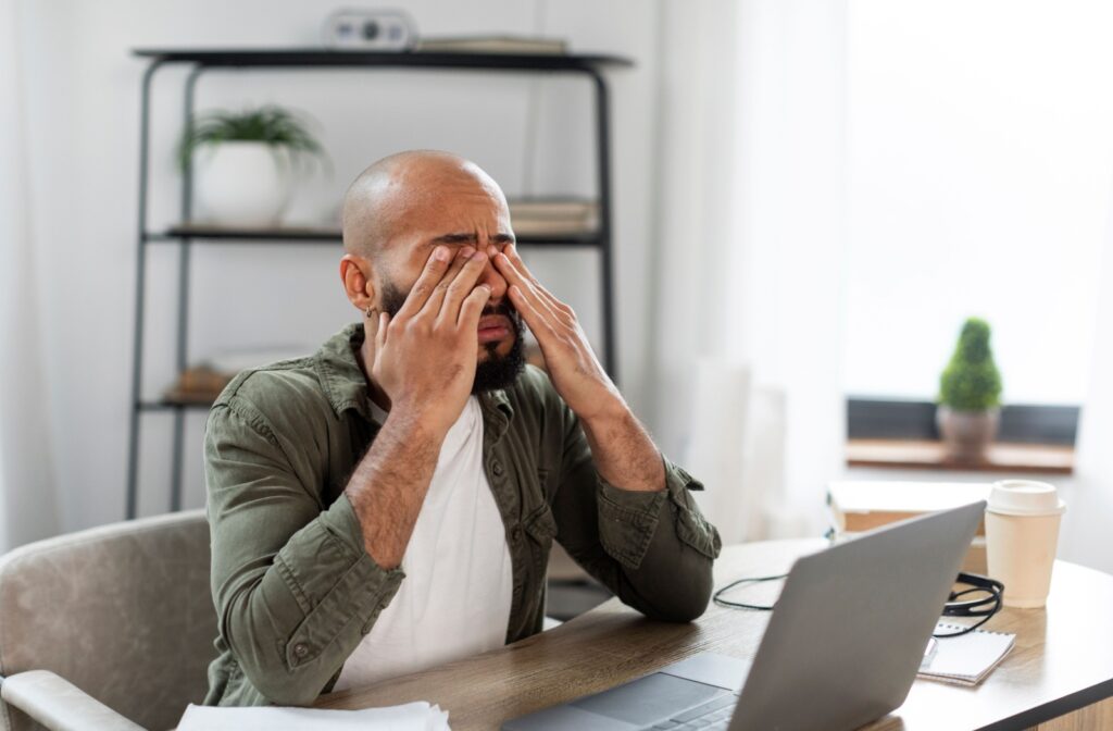 A man sitting at a computer rubs at dry eyes in an attempt to relieve symptoms while working from home.